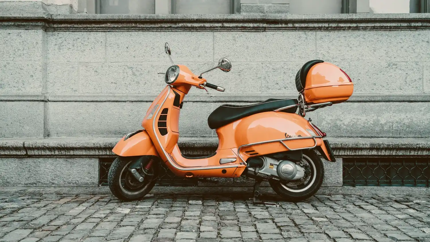 Scooter laranja estacionada na calçada de uma rua com pedras