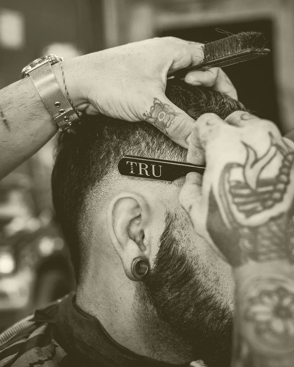 Barbeiro riscando o contorno do cabelo de um cliente tatuado